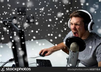 technology, gaming, entertainment, let&rsquo;s play and people concept - angry screaming young man in headset with pc computer playing game at home and streaming playthrough or walkthrough video over snow. man in headset playing computer video game at home