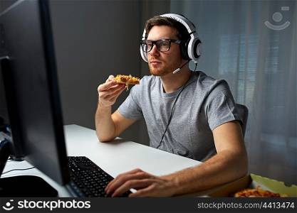 technology, gaming, entertainment, let&rsquo;s play and people concept - young man in headset with pc computer eating pizza while playing game at home and streaming playthrough or walkthrough video