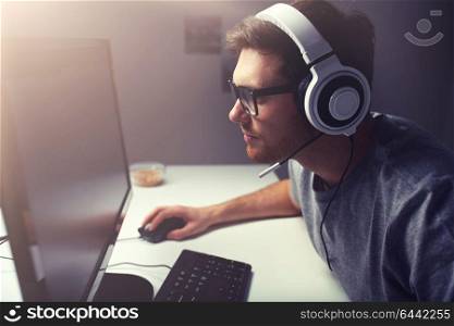 technology, gaming, entertainment, let&rsquo;s play and people concept - young man in headset and glasses with pc computer playing game at home and streaming playthrough or walkthrough video. man in headset playing computer video game at home