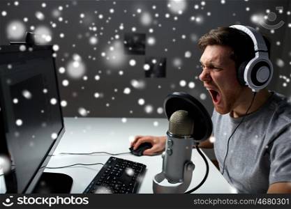 technology, gaming, entertainment, let's play and people concept - angry screaming young man in headset with pc computer playing game at home and streaming playthrough or walkthrough video over snow