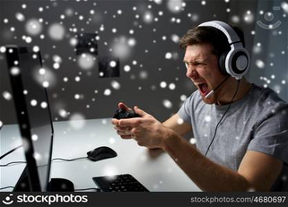 technology, gaming, entertainment, let's play and people concept - angry screaming young man in headset with controller gamepad playing computer game at home and streaming playthrough video over snow