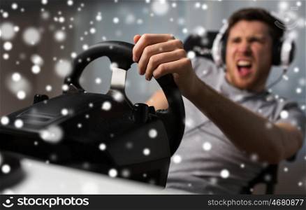 technology, gaming, entertainment, let's play and people concept - angry young man in headphones with pc computer playing car racing video game at home and steering wheel over snow