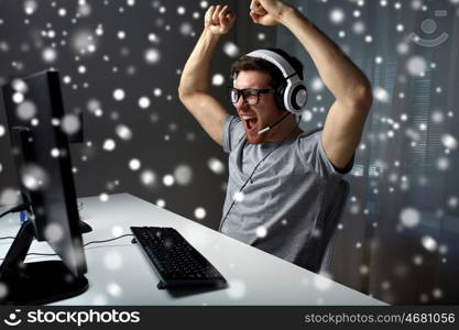 technology, gaming, entertainment, let's play and people concept - happy man in eyeglasses with headset playing and winning computer game at home and streaming playthrough walkthrough video over snow