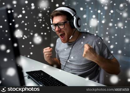 technology, gaming, entertainment, let's play and people concept - happy man in eyeglasses with headset playing and winning computer game and streaming playthrough walkthrough video at home over snow