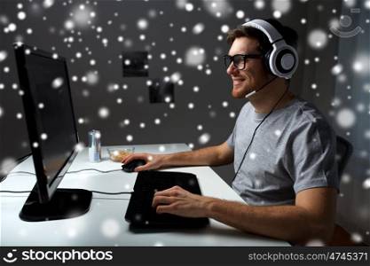 technology, gaming, entertainment, let's play and people concept - happy young man in headset and glasses with pc computer playing game at home and streaming playthrough or walkthrough video over snow