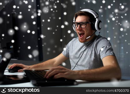 technology, gaming, entertainment, let's play and people concept - laughing young man in eyeglasses with headset playing computer game at home and streaming playthrough or walkthrough video over snow