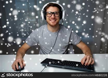 technology, gaming, entertainment, let's play and people concept - smiling young man in eyeglasses with headset playing computer game at home and streaming playthrough or walkthrough video over snow