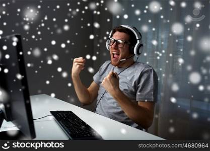 technology, gaming, entertainment, let's play and people concept - young man in eyeglasses with headset playing and winning computer game and streaming playthrough or walkthrough video over snow