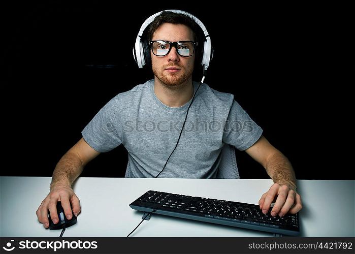 technology, gaming, let&rsquo;s play and people concept - young man or hacker in headset and eyeglasses with pc computer playing game and streaming playthrough or walkthrough video over black background