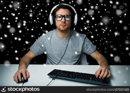 technology, gaming, let's play and people concept - man or hacker in headset and eyeglasses with pc computer playing game and streaming playthrough or walkthrough video over black background over snow