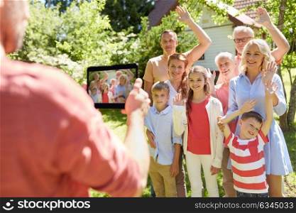 technology, generation and people concept - man taking picture of happy family by tablet pc computer in summer garden. happy family photographing by tablet pc in summer