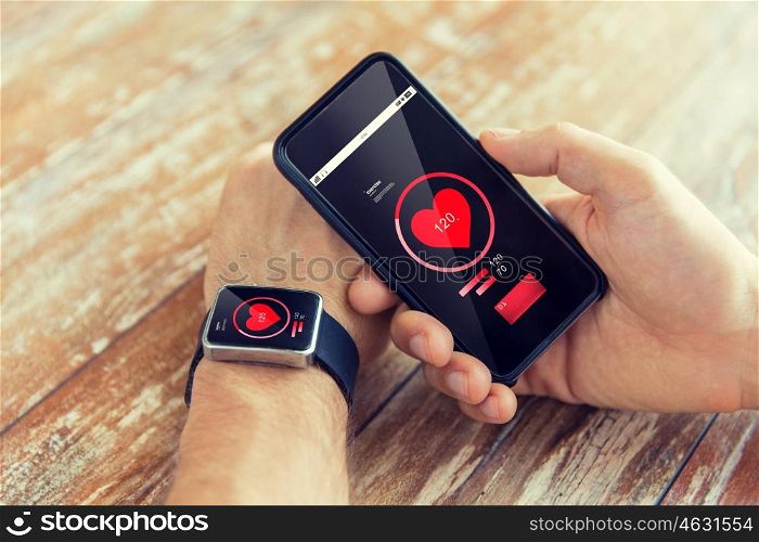 technology, health care, application and people concept - close up of male hand holding smart phone and wearing smart watch with red heart icon on screen and measuring pulse