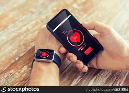 technology, health care, application and people concept - close up of male hand holding smart phone and wearing smart watch with red heart icon on screen and measuring pulse