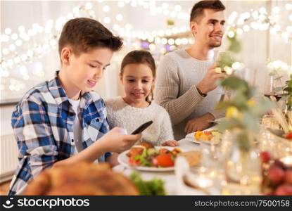 technology, holidays and people concept - happy children with smartphone at family dinner party. children with smartphone at family dinner party