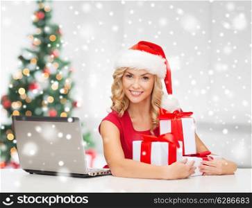 technology, holidays, online shopping and people concept - woman in santa helper hat with gift boxes and laptop computer over living room background