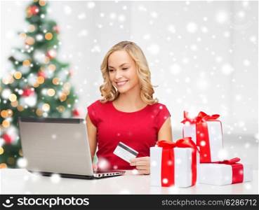 technology, holidays, online shopping and people concept - woman with credit card, gift boxes and laptop computer over living room background