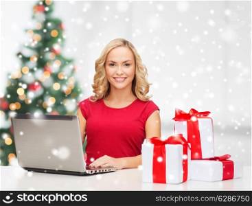 technology, holidays, online shopping and people concept - woman with gift boxes and laptop computer over living room background