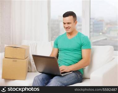 technology, home and lifestyle concept - smiling man with laptop and cardboard boxes at home