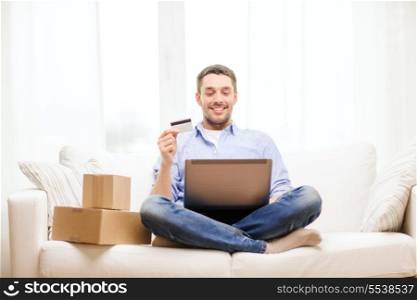 technology, home and lifestyle concept - smiling man with laptop, credit card and cardboard boxes at home
