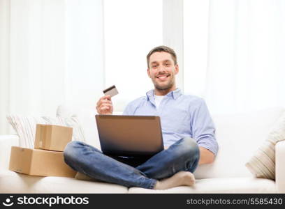 technology, home and lifestyle concept - smiling man with laptop, credit card and cardboard boxes at home