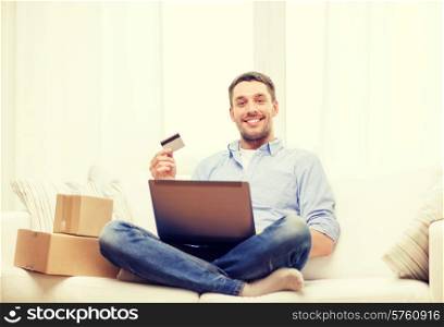 technology, home and lifestyle concept - smiling man with laptop, credit card and cardboard boxes at home