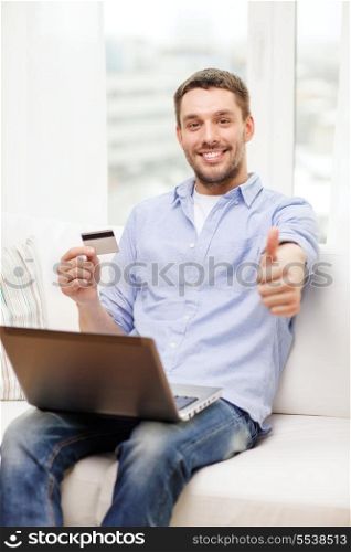 technology, home and lifestyle concept - smiling man working with laptop and credit card at home and showing thumbs up