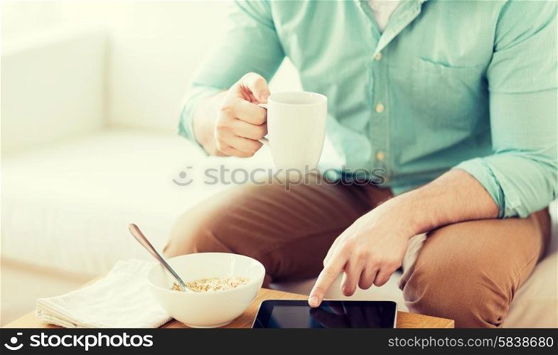 technology, home, drinks, food and lifestyle concept - close up of man with tablet pc computer and cup of coffee having breakfast at home