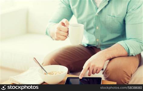 technology, home, drinks, food and lifestyle concept - close up of man with tablet pc computer and cup of coffee having breakfast at home