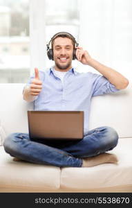 technology, home, music and lifestyle concept - smiling man with laptop and headphones at home showing thumbs up