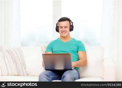 technology, home, music and lifestyle concept - smiling man with laptop and headphones at home