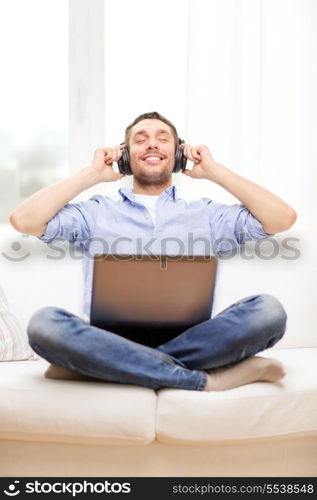 technology, home, music and lifestyle concept - smiling man with laptop and headphones at home