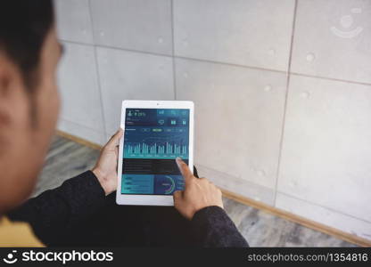 Technology in Finance and Business Marketing Concept. Graphs and Charts show on Touch Pad&rsquo;s Screen. Modern Businessman seeing Statistical Data on Digital Tablet in Office. Over the Shoulder View