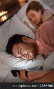 technology, internet addiction and cheat concept - man using smartphone at night while his girlfriend is sleeping. man using smartphone while girlfriend is sleeping