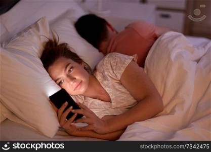 technology, internet addiction and cheat concept - woman using smartphone at night while her boyfriend is sleeping. woman using smartphone while boyfriend is sleeping