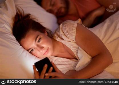 technology, internet addiction and cheat concept - woman using smartphone at night while her boyfriend is sleeping. woman using smartphone while boyfriend is sleeping