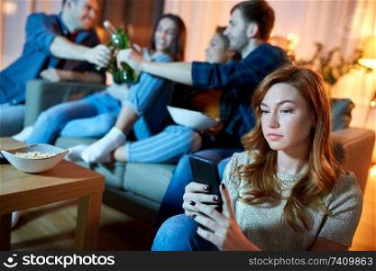 technology, internet addiction and people concept - sad young woman with smartphone at home friends party in evening. sad young woman with smartphone at home party