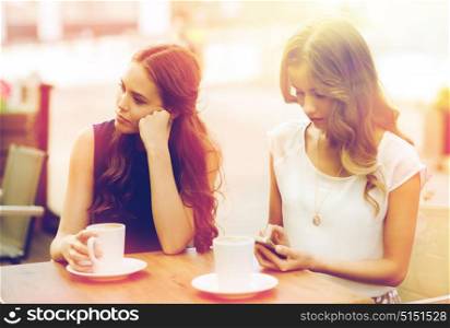 technology, internet addiction, lifestyle, friendship and people concept - young women or teenage girls with smartphones and coffee cups at cafe outdoors. women with smartphones and coffee at outdoor cafe