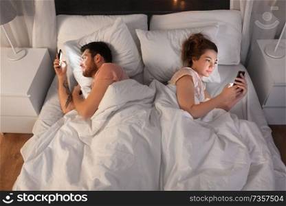 technology, internet and communication concept - couple using smartphones in bed at night. couple using smartphones in bed at night