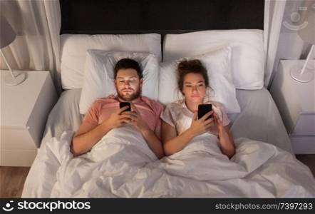 technology, internet and communication concept - couple using smartphones in bed at night. couple using smartphones in bed at night