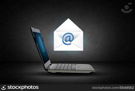 technology, internet and communication concept - open laptop computer with e-mail icon and virtual letter over dark gray background