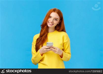 Technology, internet and gadgets concept. Cute redhead woman sending text friend, messaging, having conversation using smartphone app, smiling camera, download useful application, blue background.. Technology, internet and gadgets concept. Cute redhead woman sending text friend, messaging, having conversation using smartphone app, smiling camera, download useful application, blue background