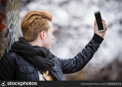 Technology internet and happiness concept. Fashionable guy taking self picture selfie with smartphone camera while walking outdoors foggy day