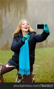 Technology internet and happiness concept. Woman content girl taking self picture selfie with smartphone camera while riding bicycle outdoors in autumn park