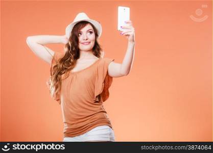 Technology internet and happiness concept. Young summer woman taking self picture selfie with smartphone camera orange background