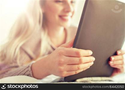 technology, internet and people concept - close up of happy young woman lying in bed with tablet pc computer at home bedroom. close up of young woman with tablet pc at home