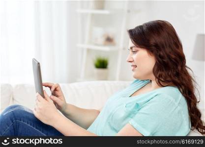 technology, internet and people concept concept - smiling young plus size woman sitting on couch with tablet pc computer at home
