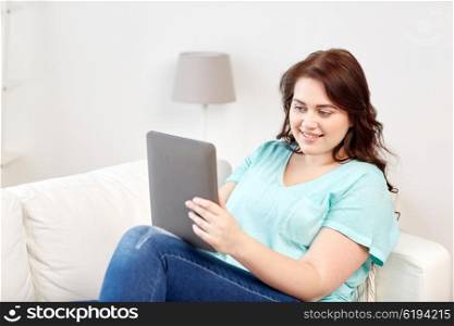 technology, internet and people concept concept - smiling young plus size woman sitting on couch with tablet pc computer at home