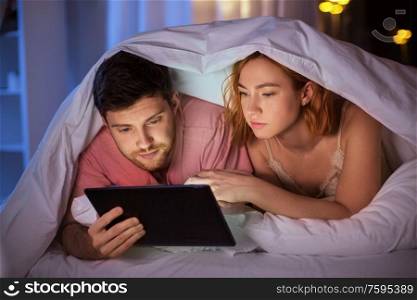 technology, internet and people concept - couple using tablet pc computer in bed at night. couple using tablet pc in bed at night