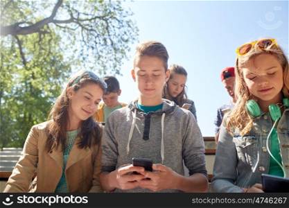 technology, internet and people concept - group of happy teenage friends with smartphone and headphones outdoors