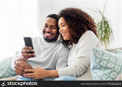 technology, internet and people concept - happy african american couple with smartphone at home. african american couple with smartphone at home